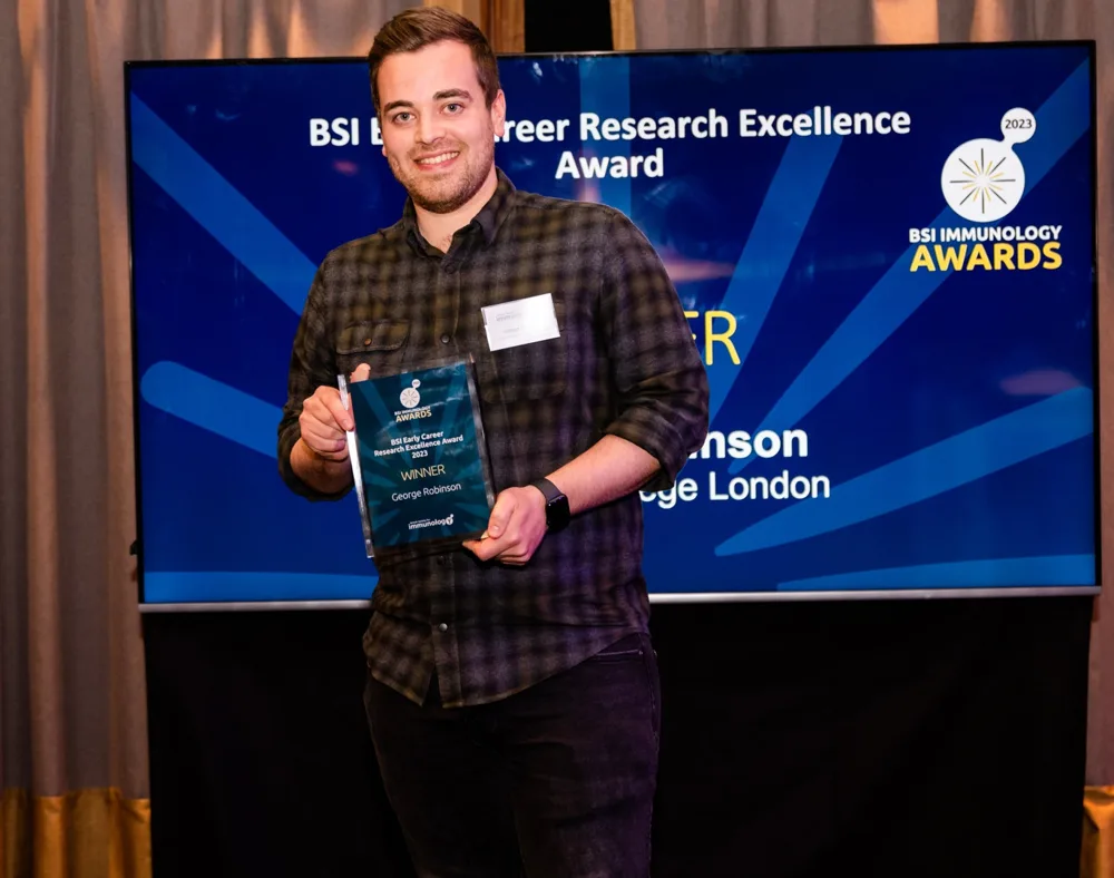 George holding his BSI Early Career Research Excellence Award plaque at the 2023 BSI Immunology Awards