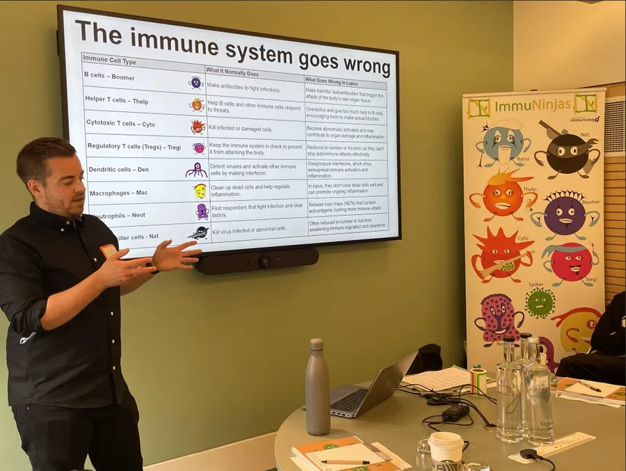 George teaching at the Understanding Lupus course, presenting a slide on how the immune system goes wrong in lupus, beside an ImmuNinjas banner